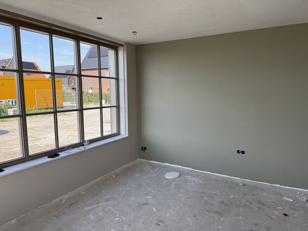 Kamer met roedenraam en een wand in zacht grijsgroen, kort na het afwerken